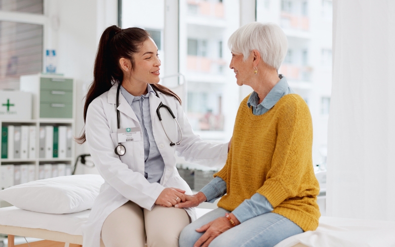 Giovane dottoressa che sta parlando con una donna adulta sul lettino del suo ambulatorio