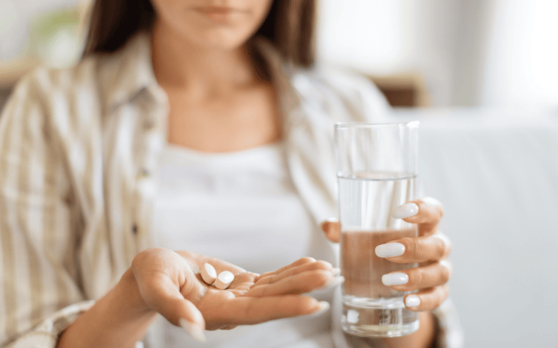 Immagine di una donna che sta tenendo in una mano un bicchiere d'acqua e nell'altra delle pastiglie